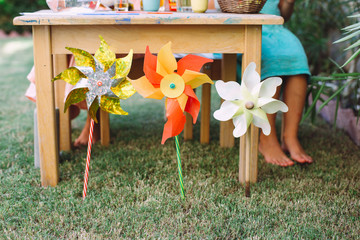 Fototapeta premium Three colorful toy windmills in the grass with kids feet on the background