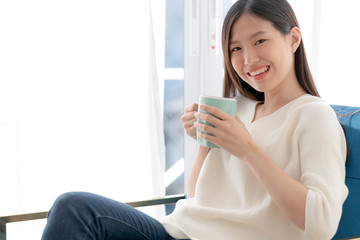 relax and peaceful asian woman enjoy vacation weekend with hot tea and good book morning time near window home background