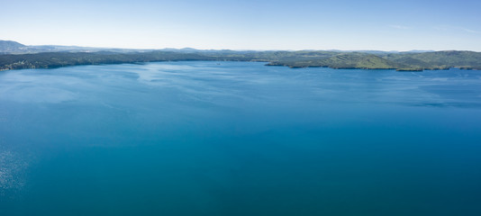 Fototapeta premium Lake with turquoise water, green trees; montain in the background; reflection in the water; beautiful summer landscape lake surrounded by forest; aerial drone shot over beautiful mountain forest lake