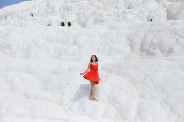 Beautiful woman in a red dress stands against the white mountains. Fabulous landscape, amazing nature. Girl on a white rock on a Sunny day