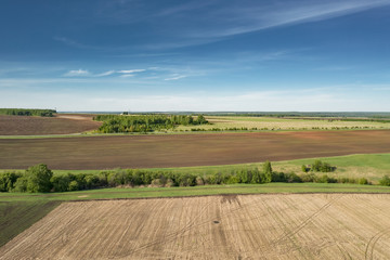 aerial footage of farmland; drone flying forward over a agricultural fields; clear boundaries of plowing the land; agricultural landscapes stretching over vast land areas, meadows and forest belts
