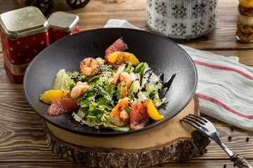 shrimp salad with sliced grapefruit, orange and lettuce on brown plate on wooden table