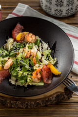 shrimp salad with sliced grapefruit, orange and lettuce on brown plate on wooden table