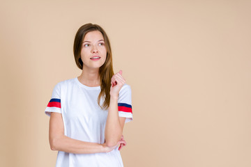 Young thoughtful woman looking away,  standing on pastel beige background