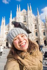 Winter travel, vacations and birds concept - Young funny woman taking selfie with pigeons near Milan Cathedral Duomo di Milano, Italy.