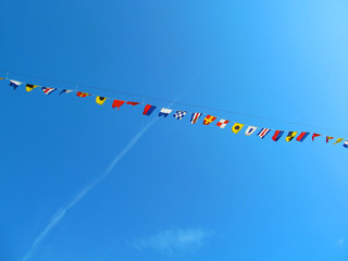 Nautical flags of sea cruise liner. Many colored marine flags hanging in one line on the rope and waving by the wind against a bright blue sky.