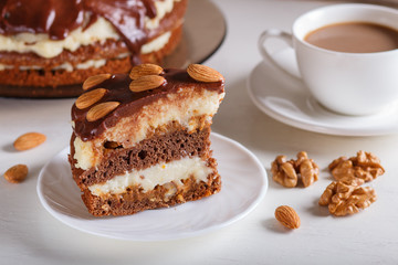Homemade chocolate cake with milk cream, caramel and almonds on white wooden background. cup of coffee.