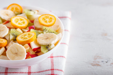 Vegetarian salad of bananas, apples, pears, kumquats and kiwi on linen tablecloth, close up, selective focus, copy space.