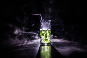 Cocktail glass splashing on dark toned smoky background or colorful cocktail in glass. Party club entertainment. Mixed light.