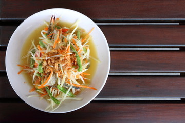 Top view, closeup papaya salad with raw blue swimming crab in white plate on wood table background is famous food in Thailand look delicious. Have copyspace.