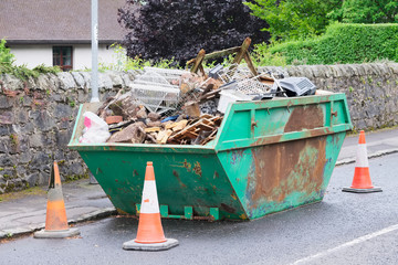 Green skip and cones outside house on road full of waste and rubbish to recycle