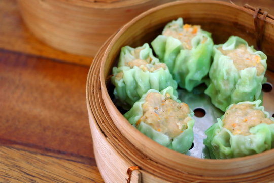 Close up Cantonese Shumai (Siu Mai) Dim Sum, shrimp & pork Chinese steamed dumplings recipe wrap by green wonton wrapper (Kanom Jeeb in Thai) on wood table background, side view have copy space.