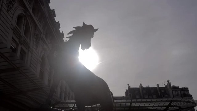 Beautiful horse sculpture in back light with a big sun in the background in Paris during the summer. Low angle 4K of parisian monument.