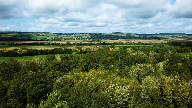 Aerial landscape forward shot over little forest cloudy bright and shady view of agricultural areas hills and little village in background summer zala county hungary europe
