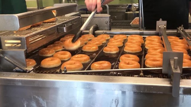 A quality control baker removing the imperfect doughnuts from a deep fat fryer. The rest are cooked to perfection. Filmed in 4k at cinematic 24 fps.