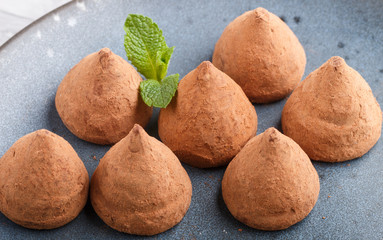 Chocolate truffle on blue ceramic plate on gray concrete background.