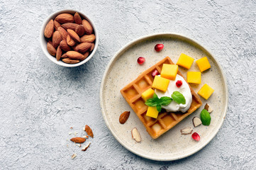 Fototapeta na wymiar Sweet breakfast with homemade waffles, fresh mango, pomegranate and mint. Top view. 