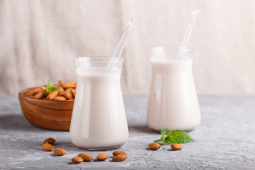 Organic non dairy almond milk in glass and wooden plate with almond nuts on a gray concrete background.