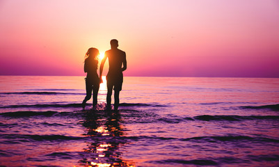Silhouette of couple in love running inside ocean water at sunset - Lovers having tender moments...