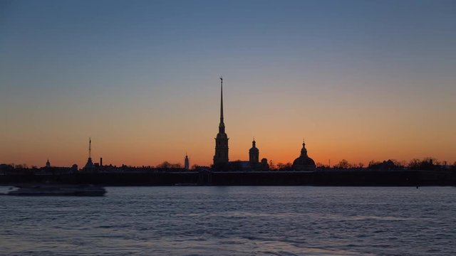 Time lapse of Peter and Paul fortress at sunset on a background of pure pink sky, night illumination lights up, darkness comes, boats and ferries pass along the Neva river, St. Petersburg, Russia