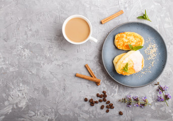 Cheese pancakes on a blue ceramic plate and a cup of coffee on a gray concrete background. copy space.