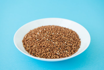 Plate with raw buckwheat on a blue background