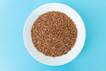 Plate with raw buckwheat on a blue background