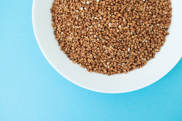 Plate with raw buckwheat on a blue background