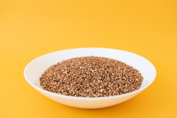 Plate with raw buckwheat on yellow background