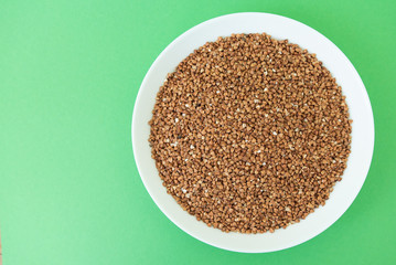 Plate with raw buckwheat on green background