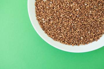 Plate with raw buckwheat on green background