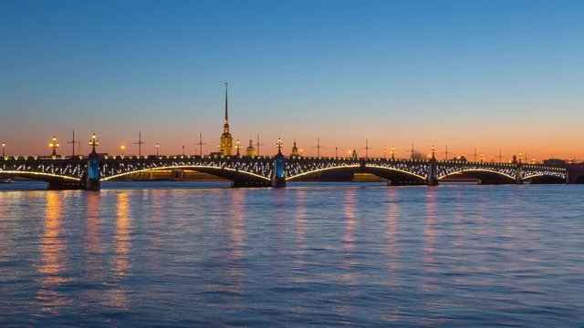 Timelapse of Trinity Bridge (Troitskiy Most) over the Neva river and Peter and Paul fortress at sunset, darkness comes, night illumination lights up, reflection in the water, St. Petersburg, Russia