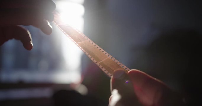 Close Up Hands Holding Up Old Film Strip To The Light And Looking At The Cells With Lens Flare