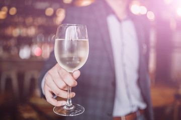 A young man holding a glass of white wine. Restaurant, catering, hospitality and beverage concept.