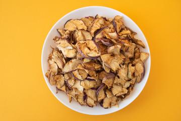 dried apples in white plate on yellow background