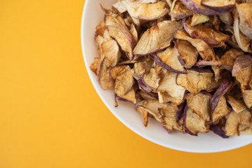 dried apples in white plate on yellow background