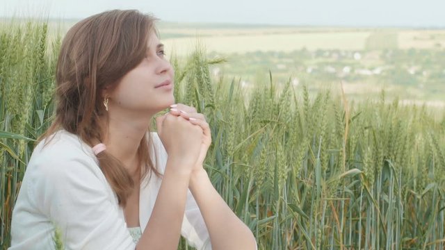 young girl praying words of prayer out and looking at the sky in a field , a woman among cereal spikelets enjoying nature and thanks God, the concept of religion and faith