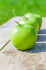 Freshly cropped geen apples on wooden table over grenn grass background.