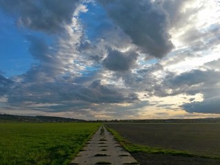 Road made of concrete panels, between fields, loses in the distance, with a cloudy sky