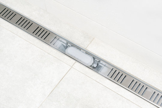 Linear shower drain system. With transparent grate to show internal siphon and all system. Shower drain channel. Shower floor drain. Tile. Drainage at bathroom. Repair