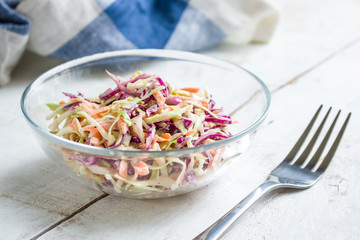 fresh coleslaw salad in glass bowl and fork on wooden table