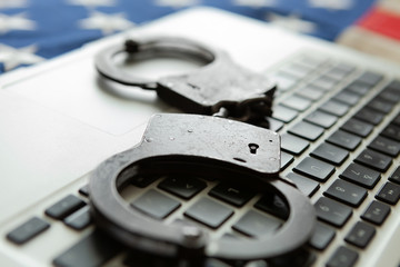Handcuffs over a laptop with an old USA flag on background - close up studio shot