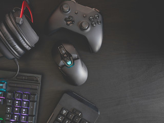 gamer workspace concept, top view a gaming gear, mouse, keyboard, joystick, headset, mobile joystick and mouse pad on black table background with RGB color.