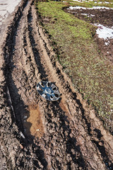a cap with a car wheel lies on a dirty, broken dirt road in the city after a rain