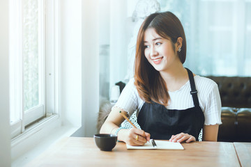 Portrait of young beautiful woman writing on notebook with cup of coffee on wooden table