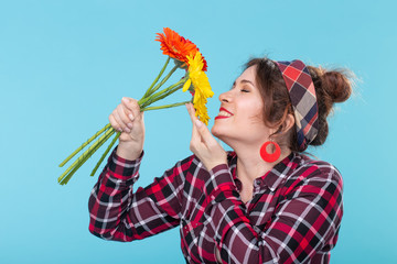 Beautiful positive young woman in a plaid shirt and a bandage sniffing beautiful bright gerbera...