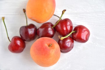 Juicy red cherries and fresh tasty apricot with selective focus on textured neutral background. Seasonal fruits and berries. Harvest of apricot and sweet cherries on white table. Picking summer fruits