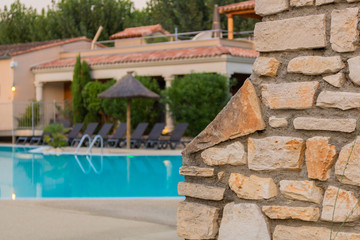 Brick wall with natural stones at the swimming pool of a touristic holiday resort in southern france. Beautifully blue water in the ppol, sun layers and sun umbrella along the poolside.