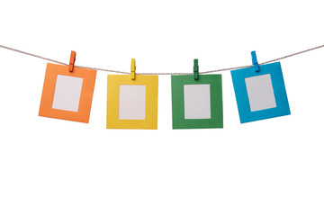 Four multicolored paper photo frames hanging on the rope with wooden clothespins isolated on white...