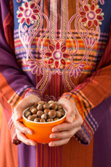 the woman wearing traditional clothes holds hazelnuts in the bowl.